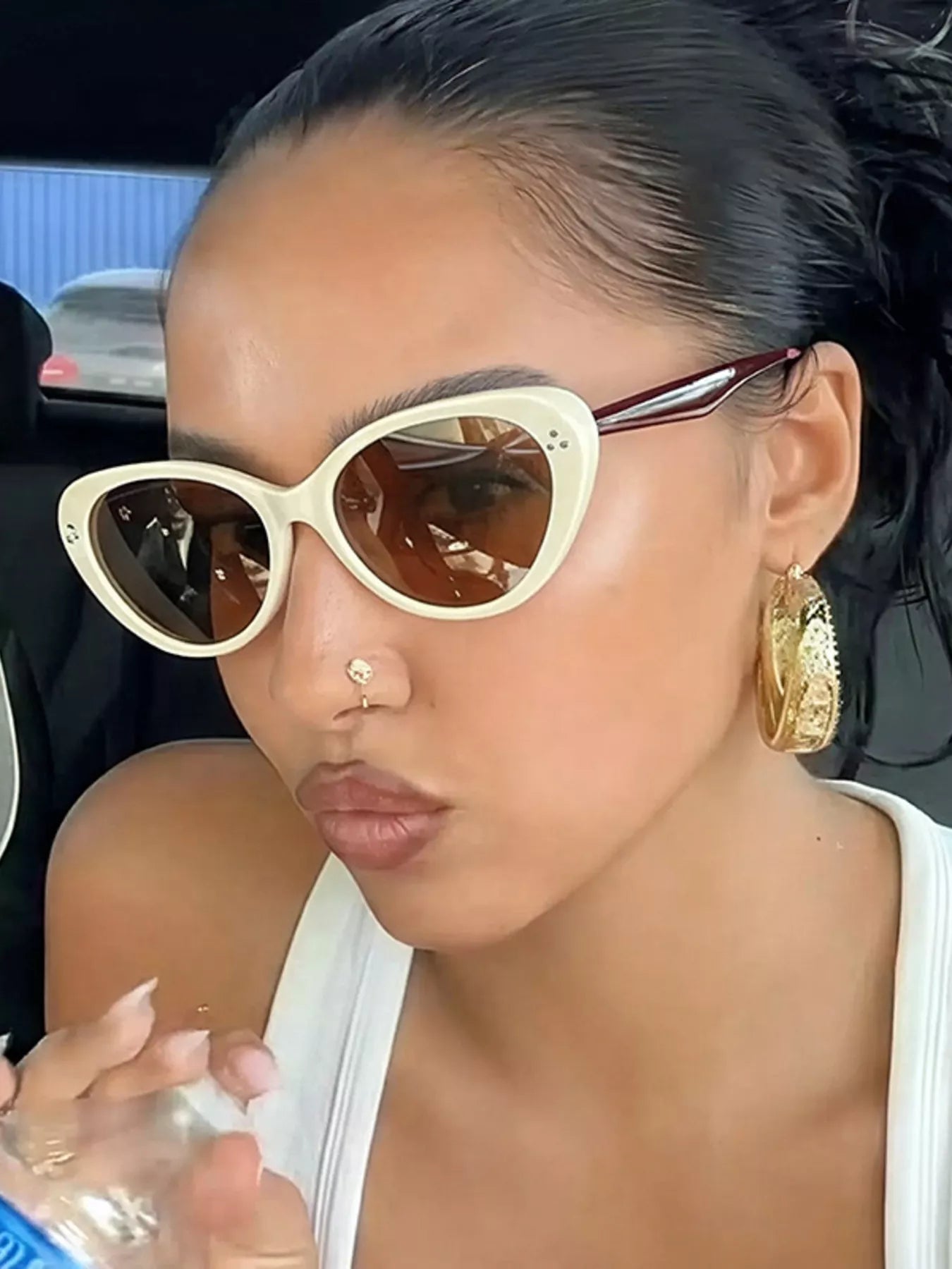 Woman wearing cream cat-eye sunglasses and gold hoop earrings.