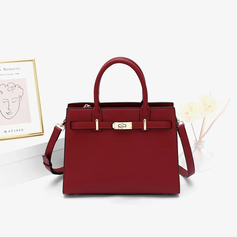 Elegant red structured handbag with gold hardware, top handles, and shoulder strap on a white surface