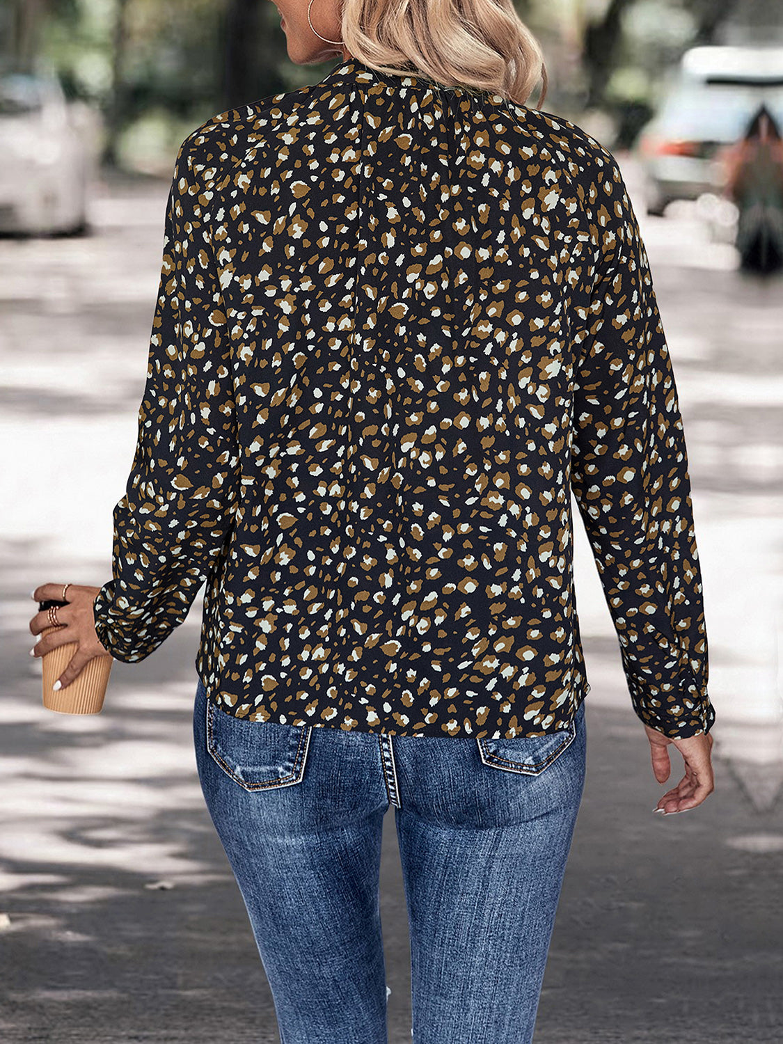 Woman wearing leopard print long sleeve blouse with jeans, walking outdoors