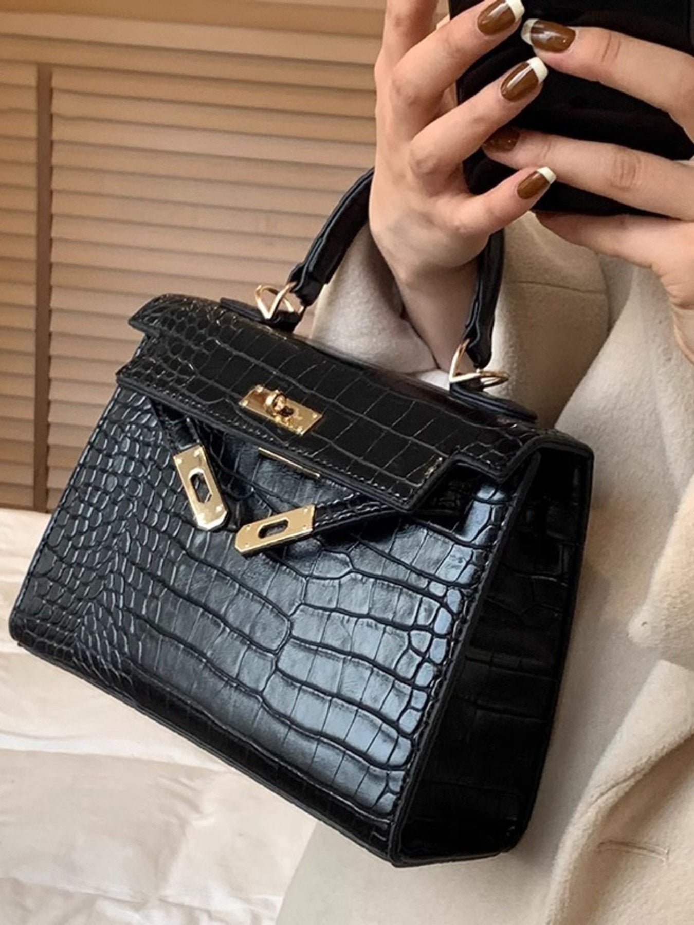 Woman holding a black crocodile-embossed handbag with gold hardware, stylish nails visible