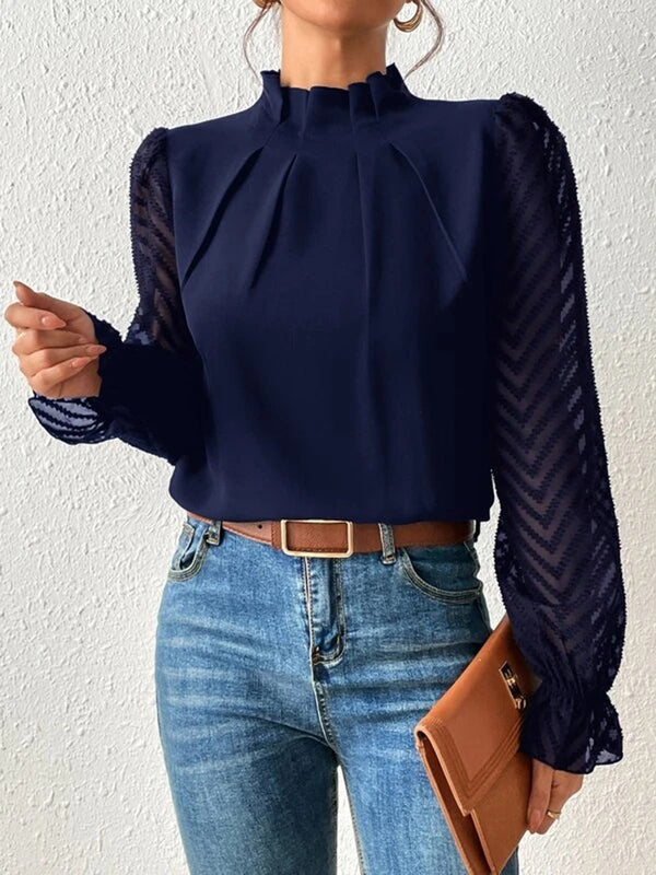 Woman wearing a navy blouse with sheer chevron sleeves, blue jeans, and holding a brown clutch