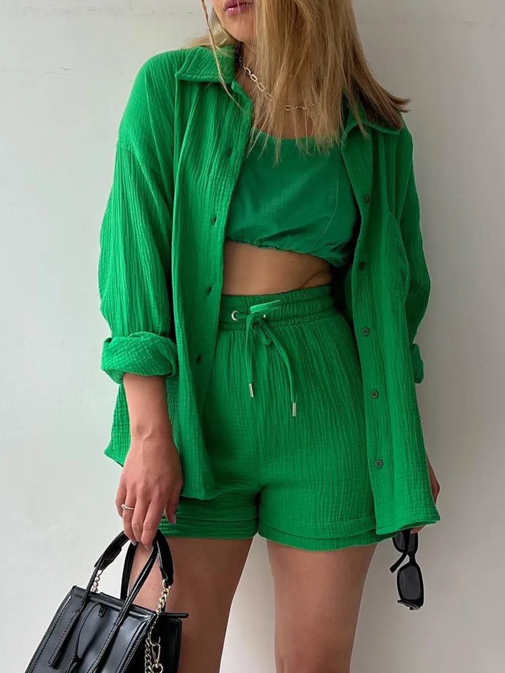 Woman in a green matching set with button-up shirt, crop top, and shorts, holding a black handbag