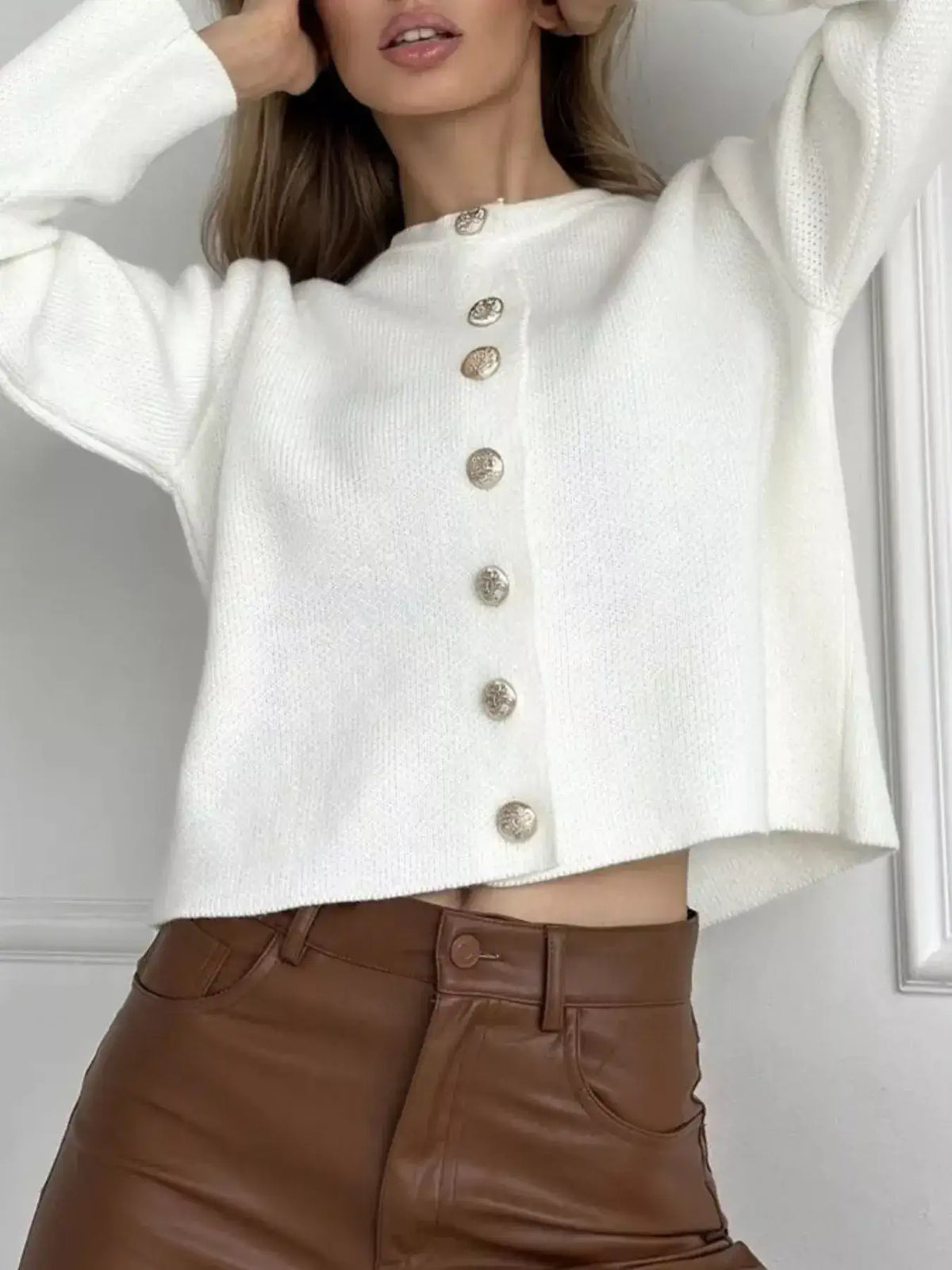 Woman wearing a white crew neck button-down cardigan by Evie's Dreamland with brown leather pants.