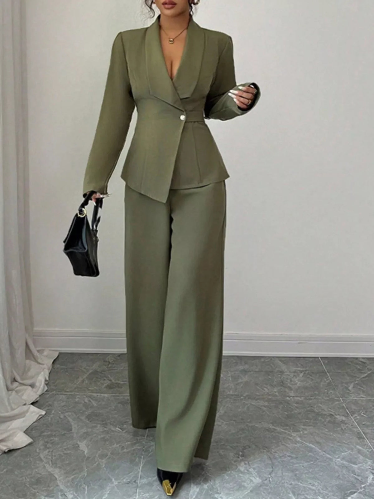 Woman wearing an olive green tailored pantsuit with wide-leg trousers and a black purse