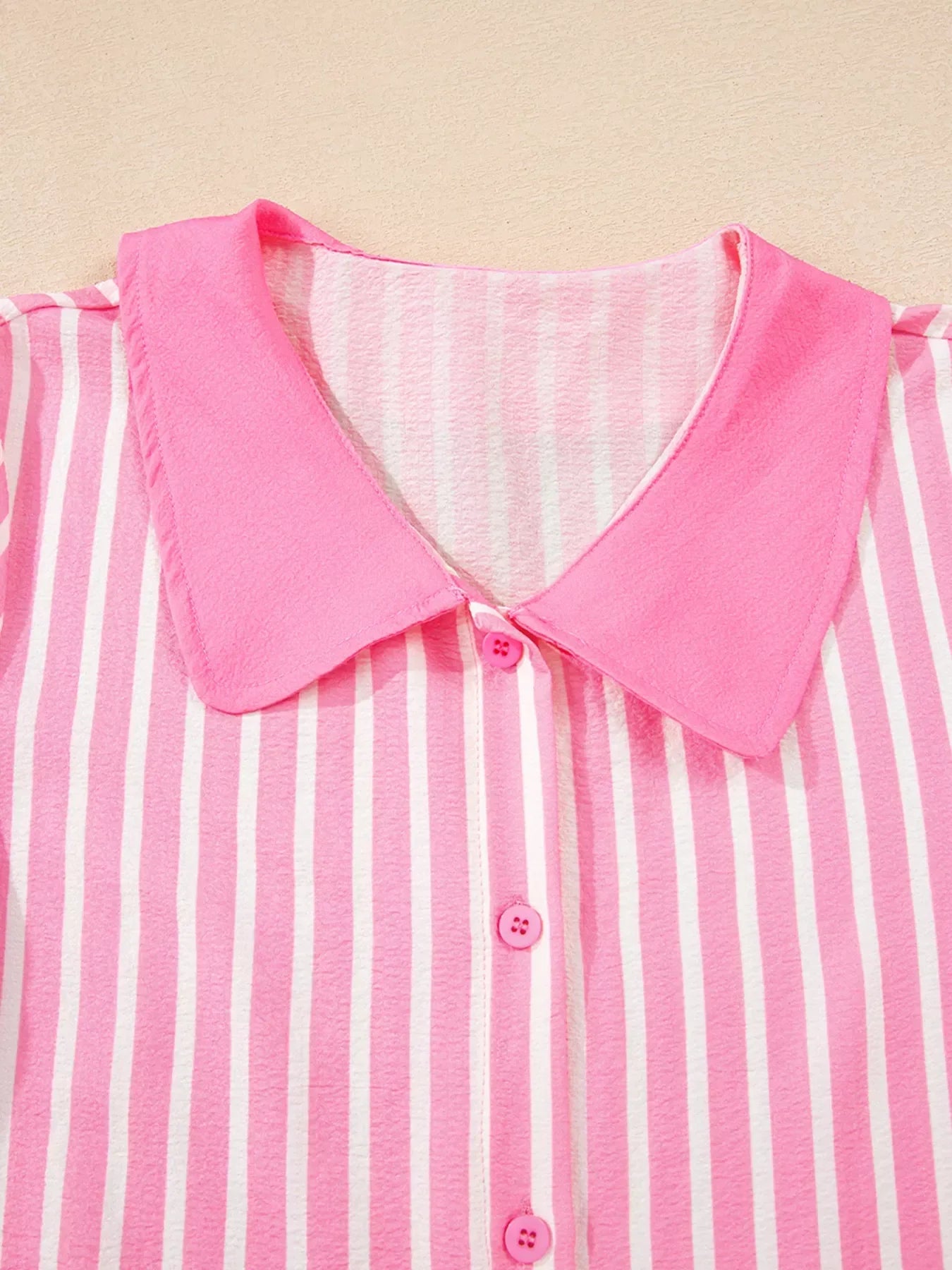 Close-up of pink and white striped button-up shirt with solid pink pointed collar on beige background