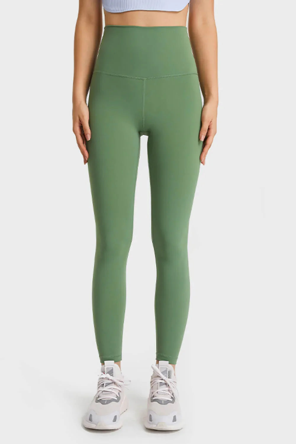 Front view of woman wearing high-waist green workout leggings and white sneakers
