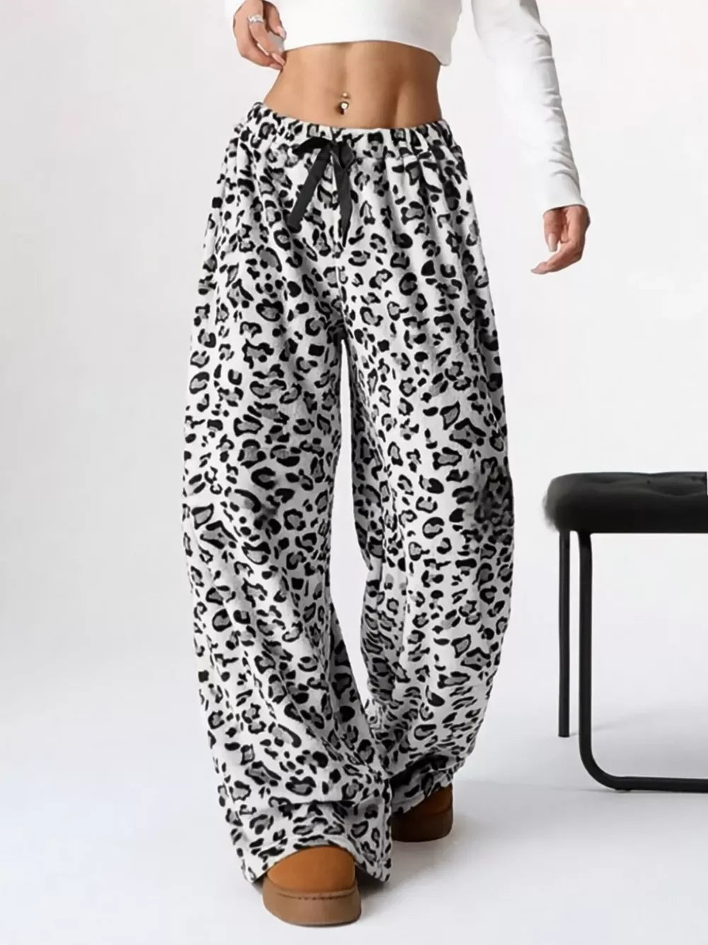Woman wearing wide-leg leopard print lounge pants with drawstring and brown boots, styled with a white crop top