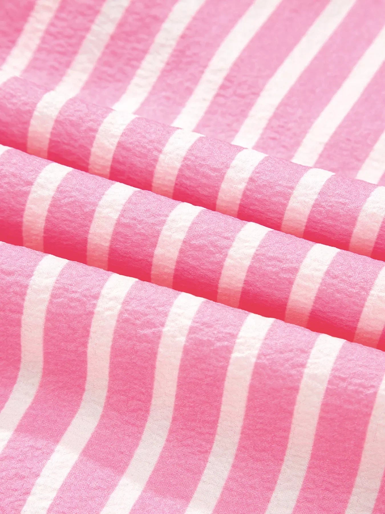 Close-up of soft pink fabric with white vertical stripes, folded with textured detail