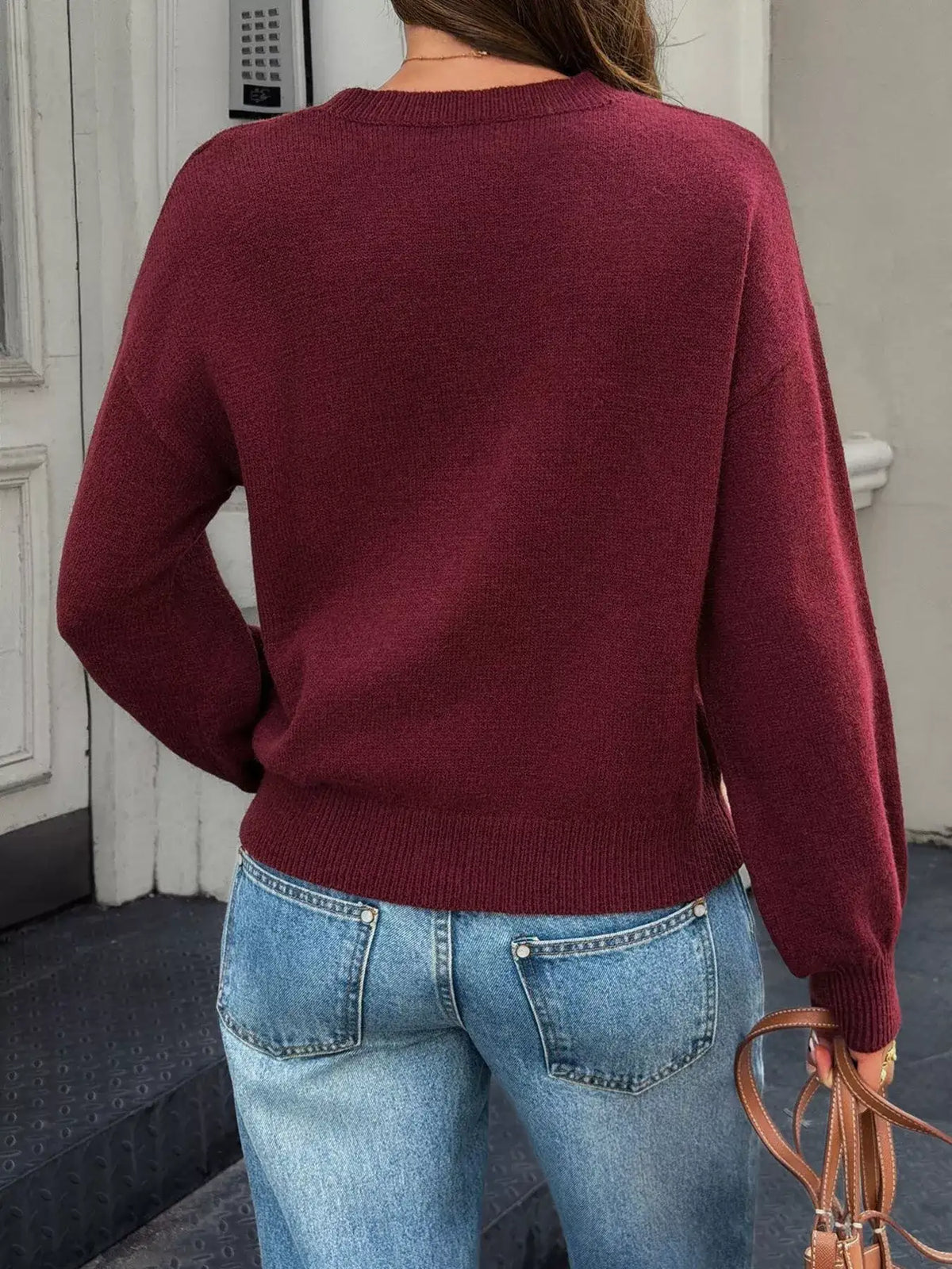 Back view of a women's burgundy crew neck dropped shoulder sweater paired with blue jeans.