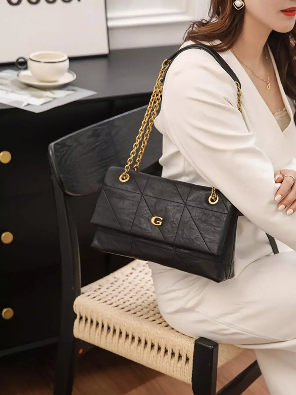 Woman in a white outfit wearing a black geometric quilted shoulder bag with a gold chain strap