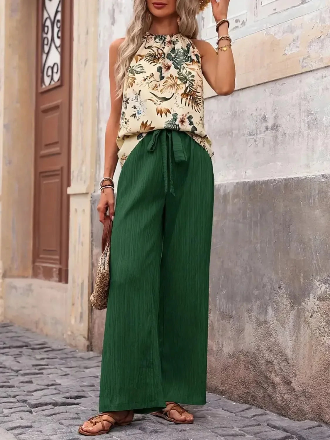 Woman wearing sleeveless floral blouse and high-waisted green wide-leg pants outdoors