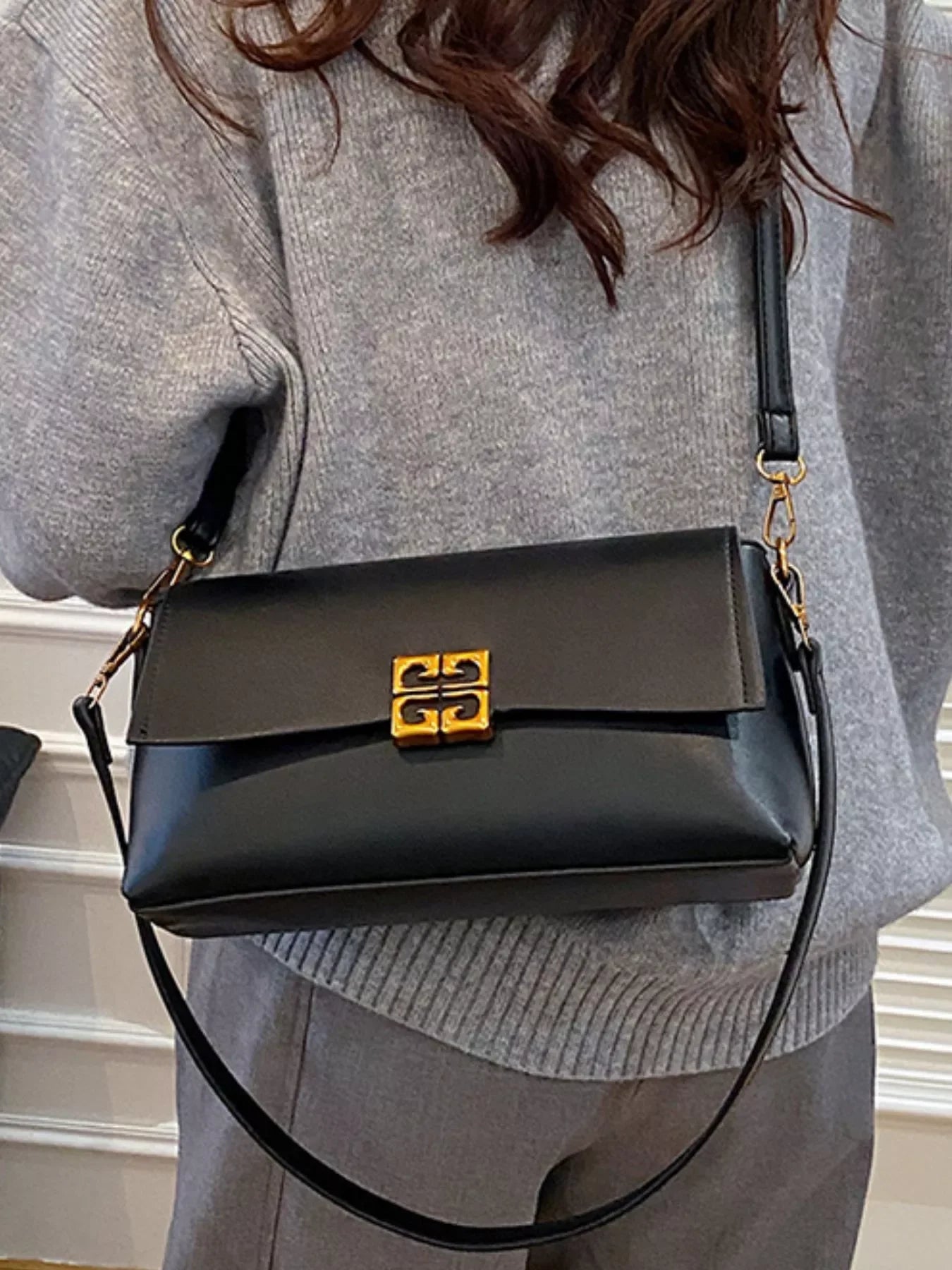 Black leather shoulder bag with gold clasp, worn by a person in gray knit sweater and pants