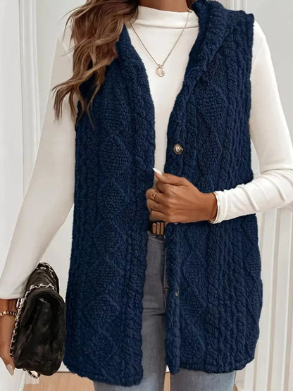 Woman wearing navy blue textured sleeveless vest over white long sleeve top holding black handbag