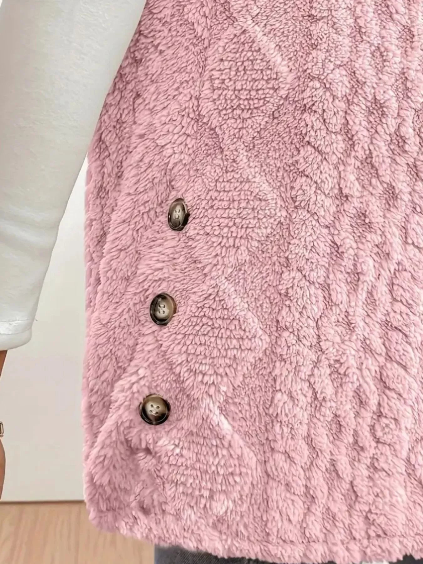 Close-up of pink textured fleece vest with three buttons over white sleeve top