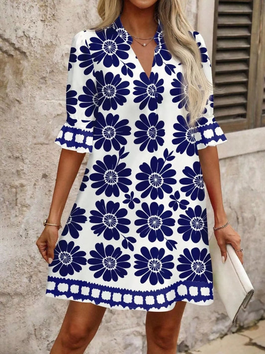 Woman wearing white shift dress with large navy floral print and ruffled sleeves holding white clutch