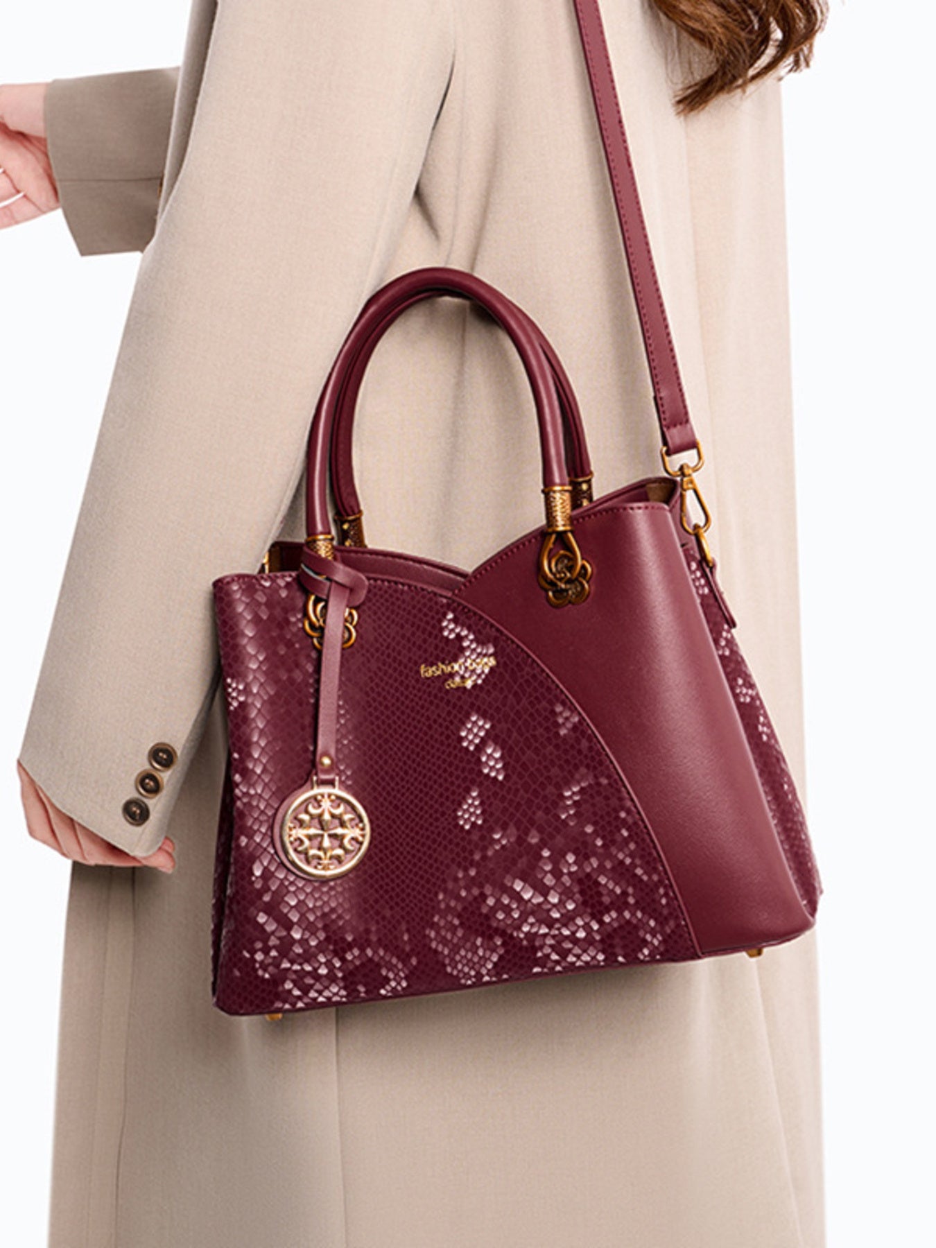 Burgundy snakeskin-patterned handbag with gold hardware, worn over a beige coat