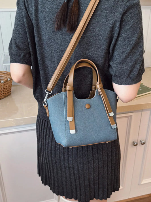 Woman wearing dark gray knit dress with blue tote handbag featuring tan leather straps indoors