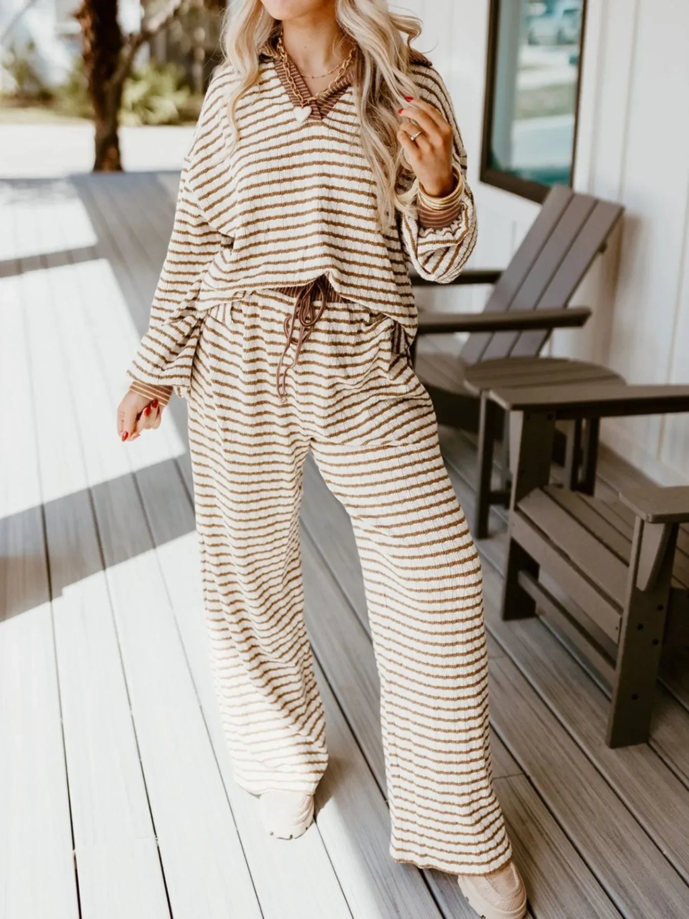 Woman wearing cozy beige and brown striped matching sweater and pants set on wooden porch