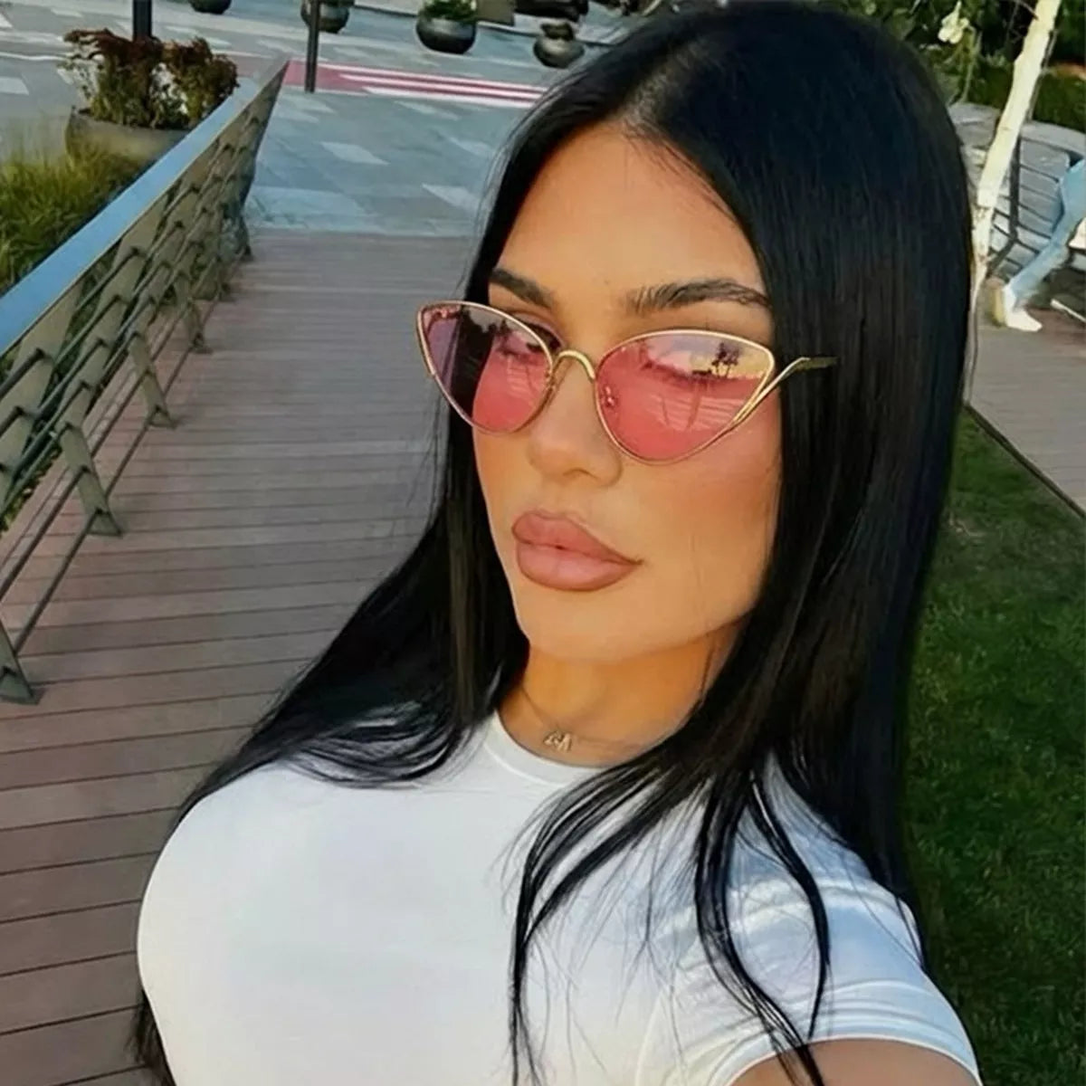 Woman with long black hair wearing pink cat-eye sunglasses and a white t-shirt.