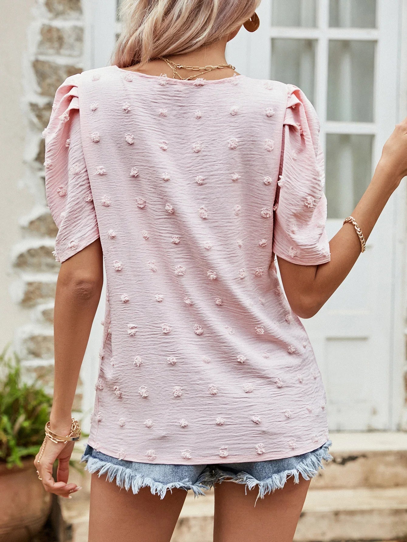 Woman wearing pink textured top with puff sleeves and blue frayed denim shorts outdoors