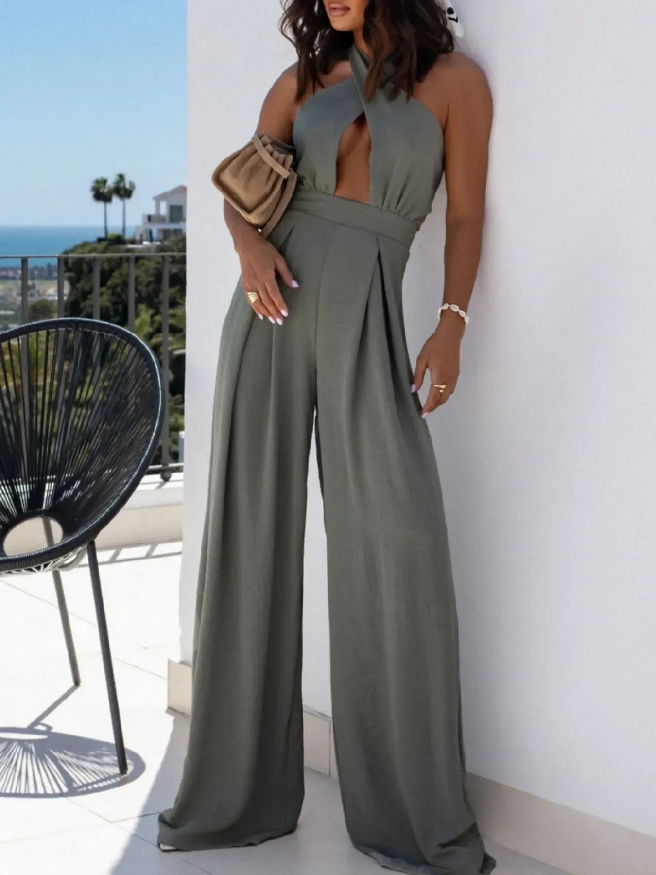 Woman wearing stylish olive green halter neck wide-leg jumpsuit on balcony with ocean view