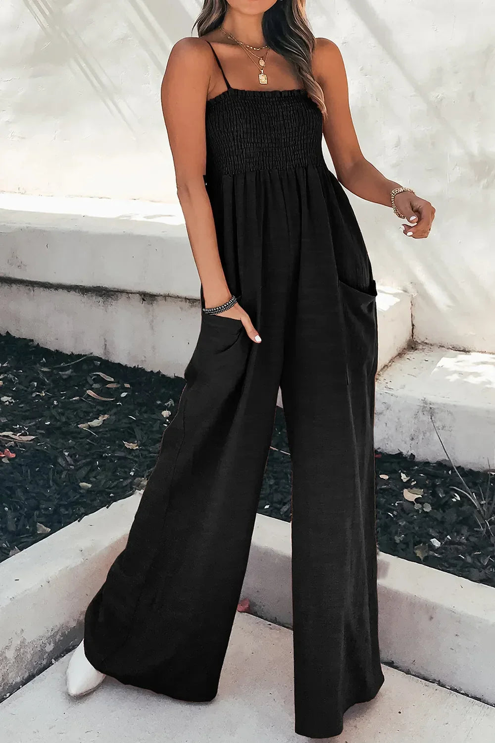 Woman wearing a black smocked strapless jumpsuit with wide legs and pockets outdoors