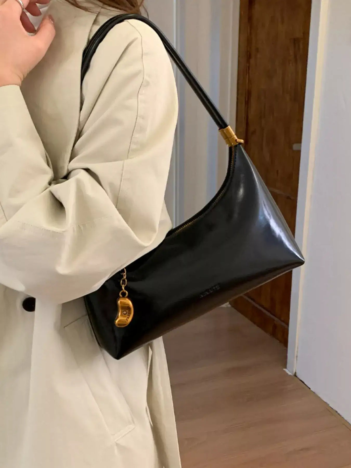 Evie's Dreamland black PU leather shoulder bag with gold charm, styled with a beige trench coat.