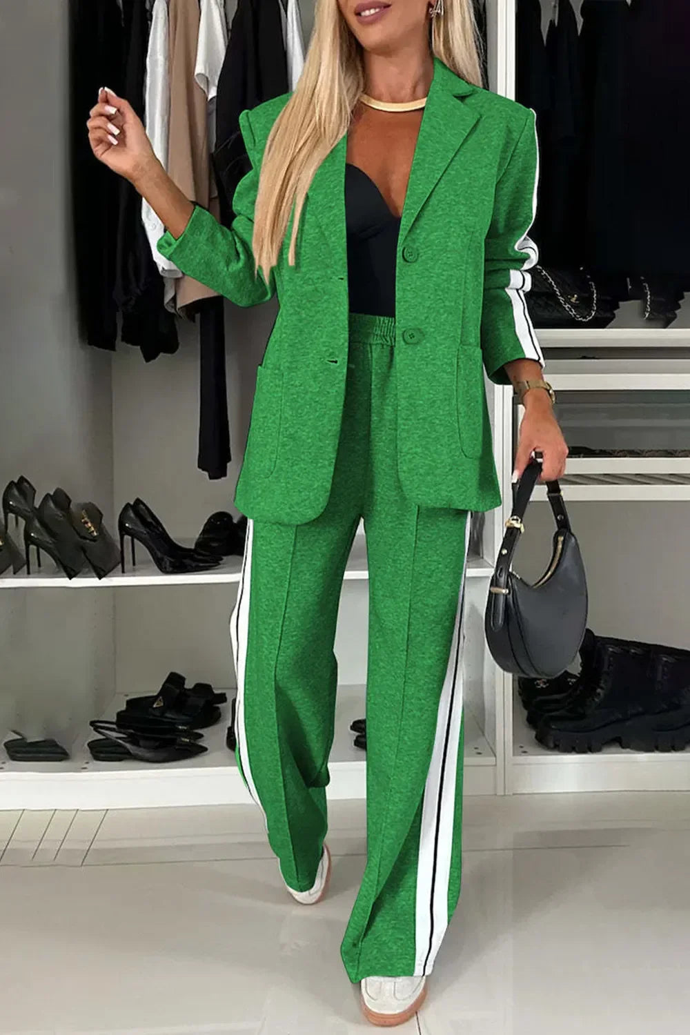 Woman wearing green blazer and matching pants with white side stripes, holding black handbag indoors
