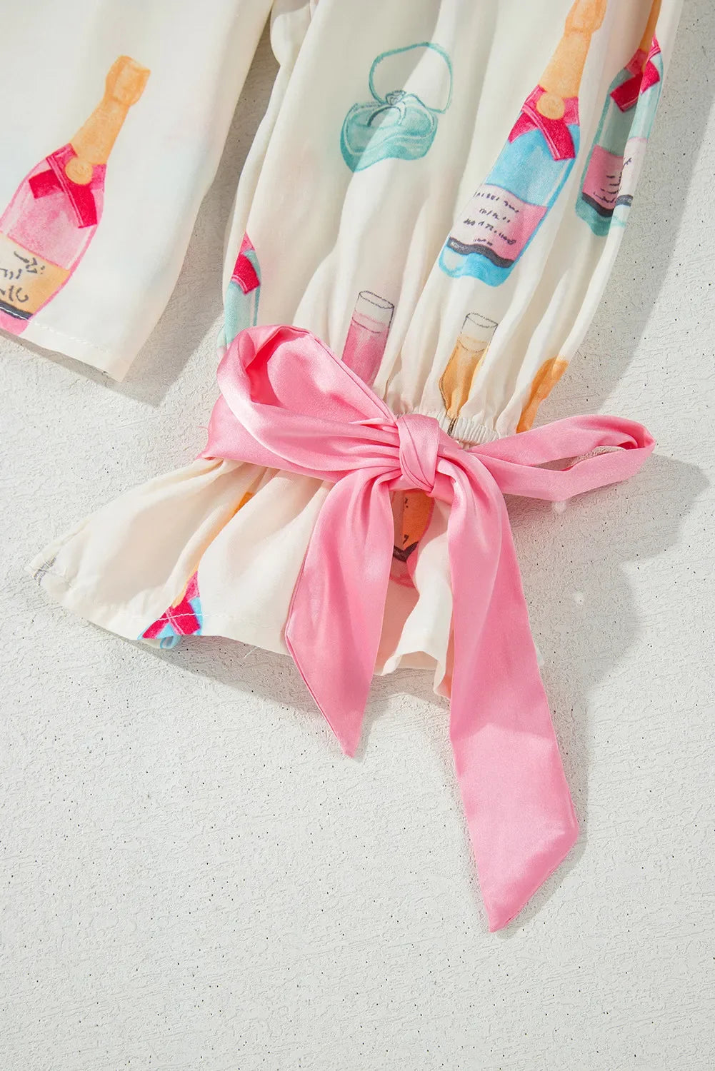 Close-up of cream fabric with colorful champagne bottle prints and a tied pink satin bow detail
