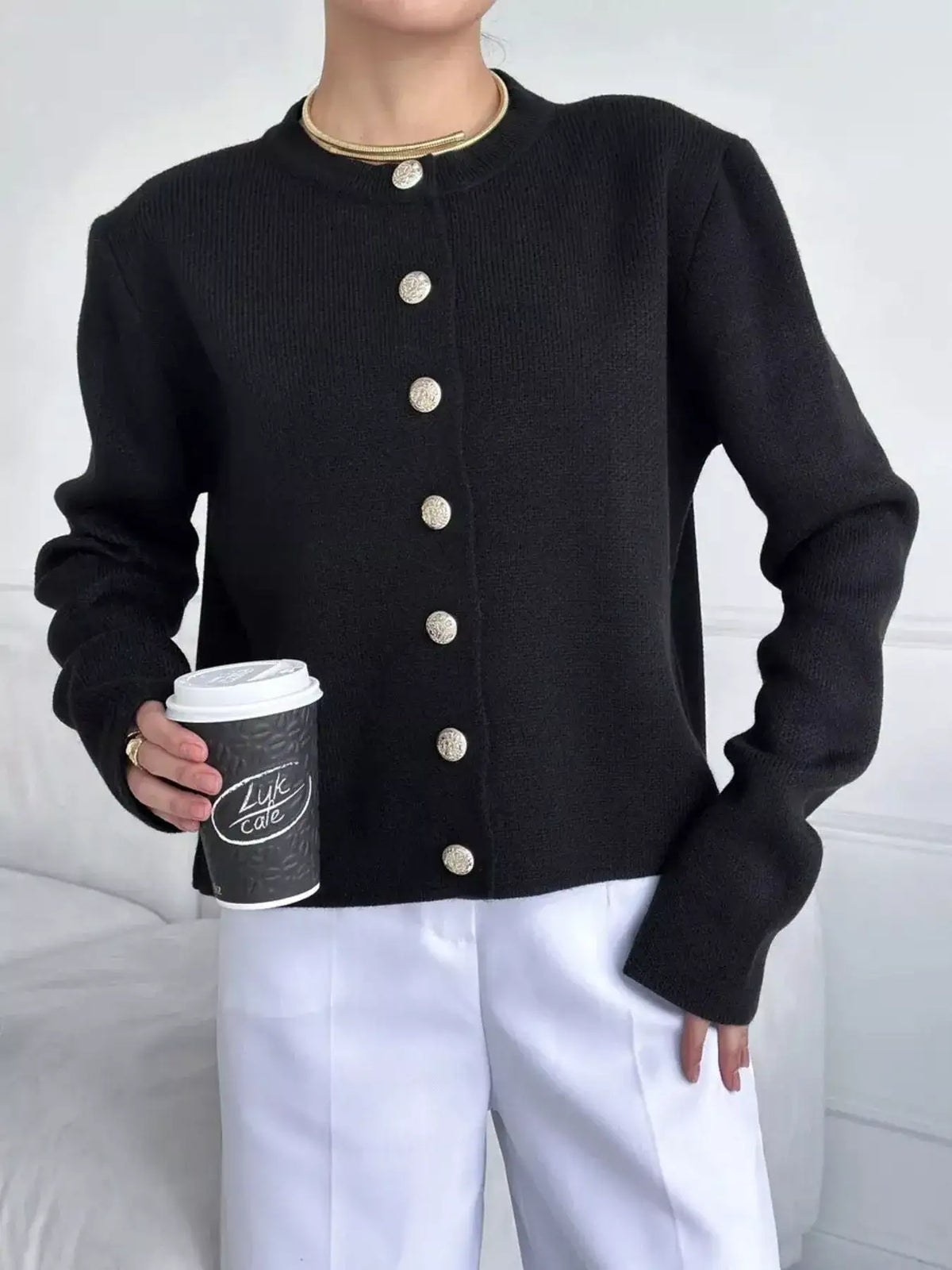 Evie's Dreamland black crew neck button down cardigan with gold buttons paired with white trousers.