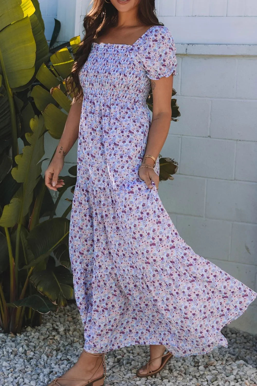 Woman wearing a flowy purple floral maxi dress with puff sleeves, standing outside by plants