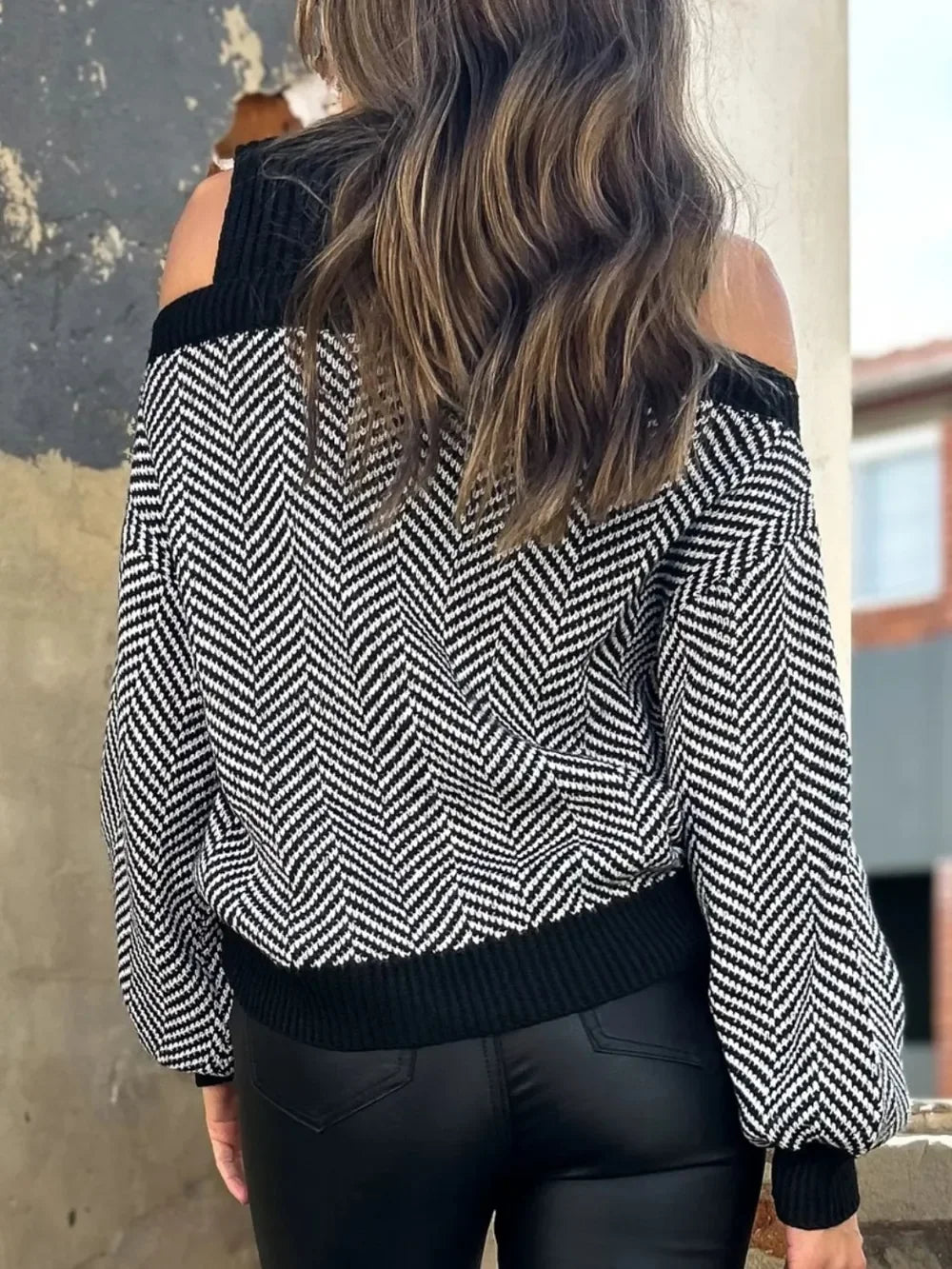 Woman wearing black and white herringbone cold shoulder sweater and black leather pants outdoors