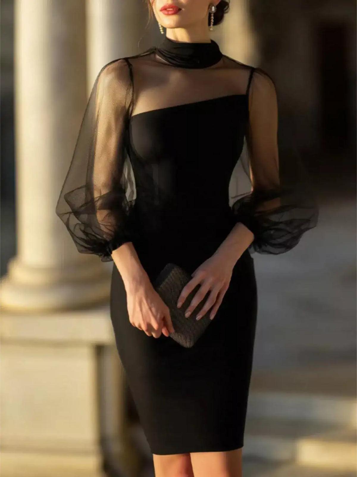 Woman wearing a black mock neck bodycon dress with sheer puff sleeves, paired with a small clutch.