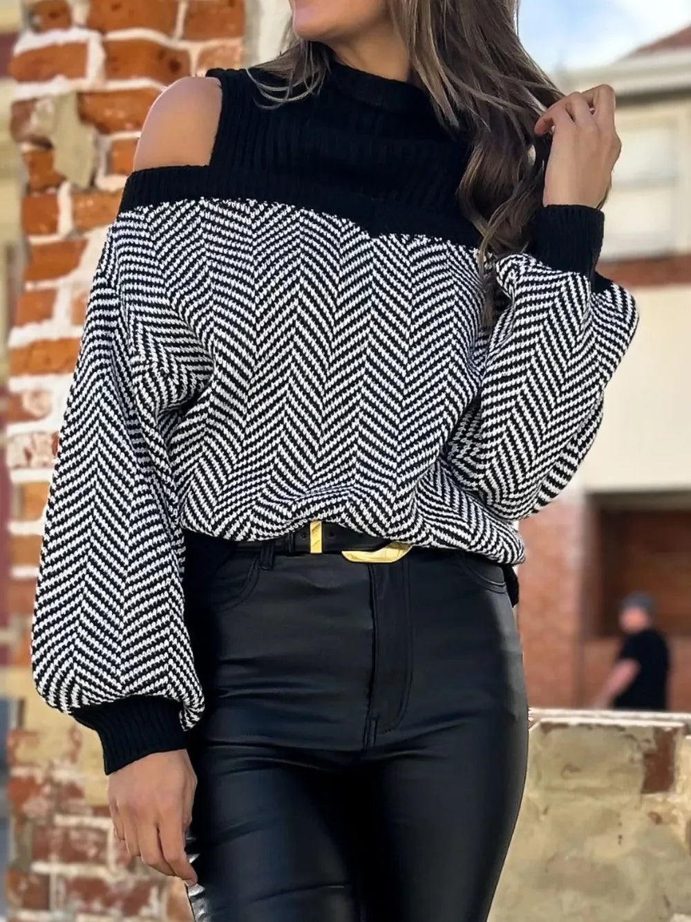 Woman wearing black and white chevron knit cold-shoulder sweater with black high-waisted pants outdoors