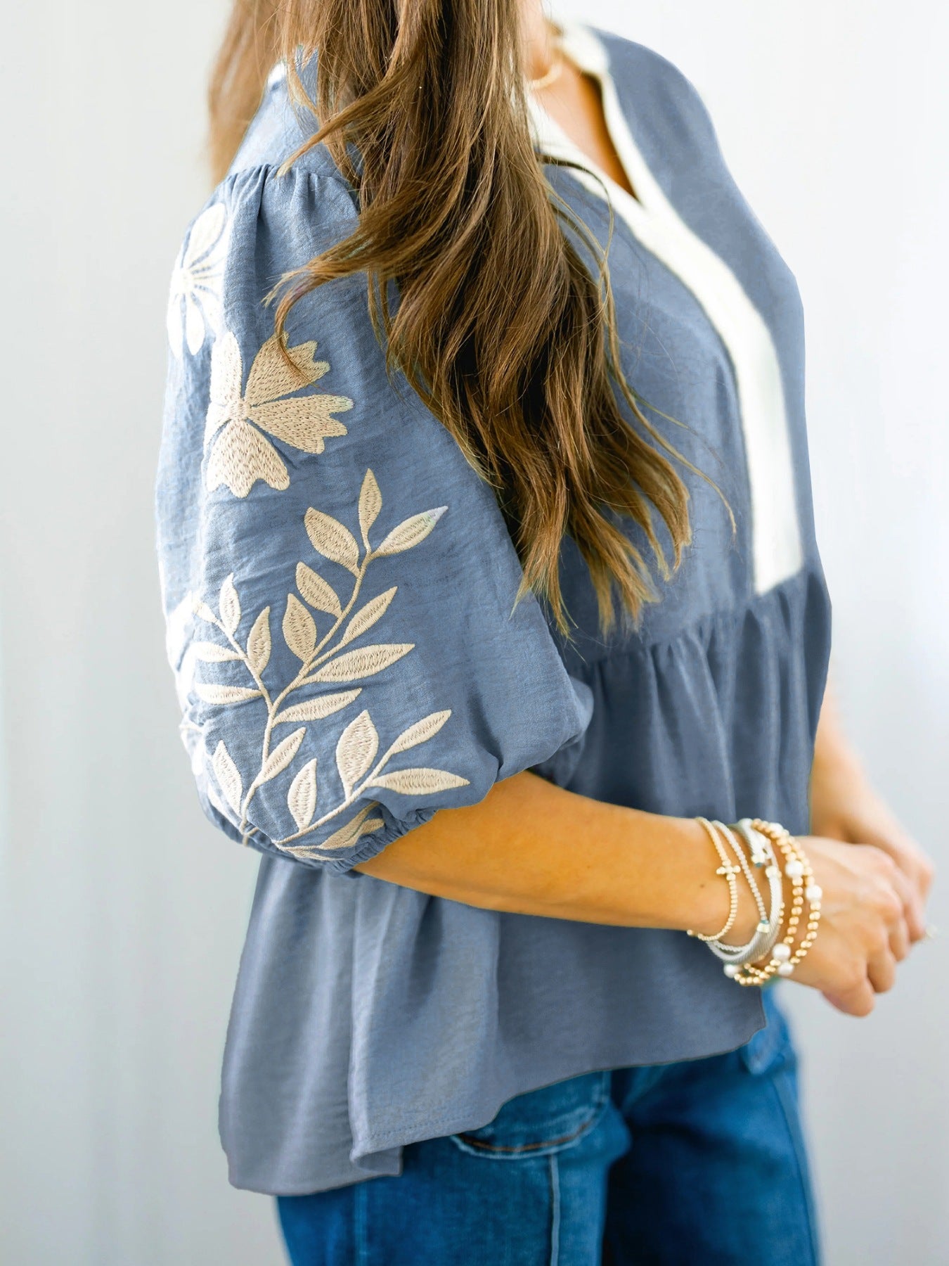 Blue embroidered blouse with floral sleeve details, styled with denim and layered bracelets for everyday elegance.