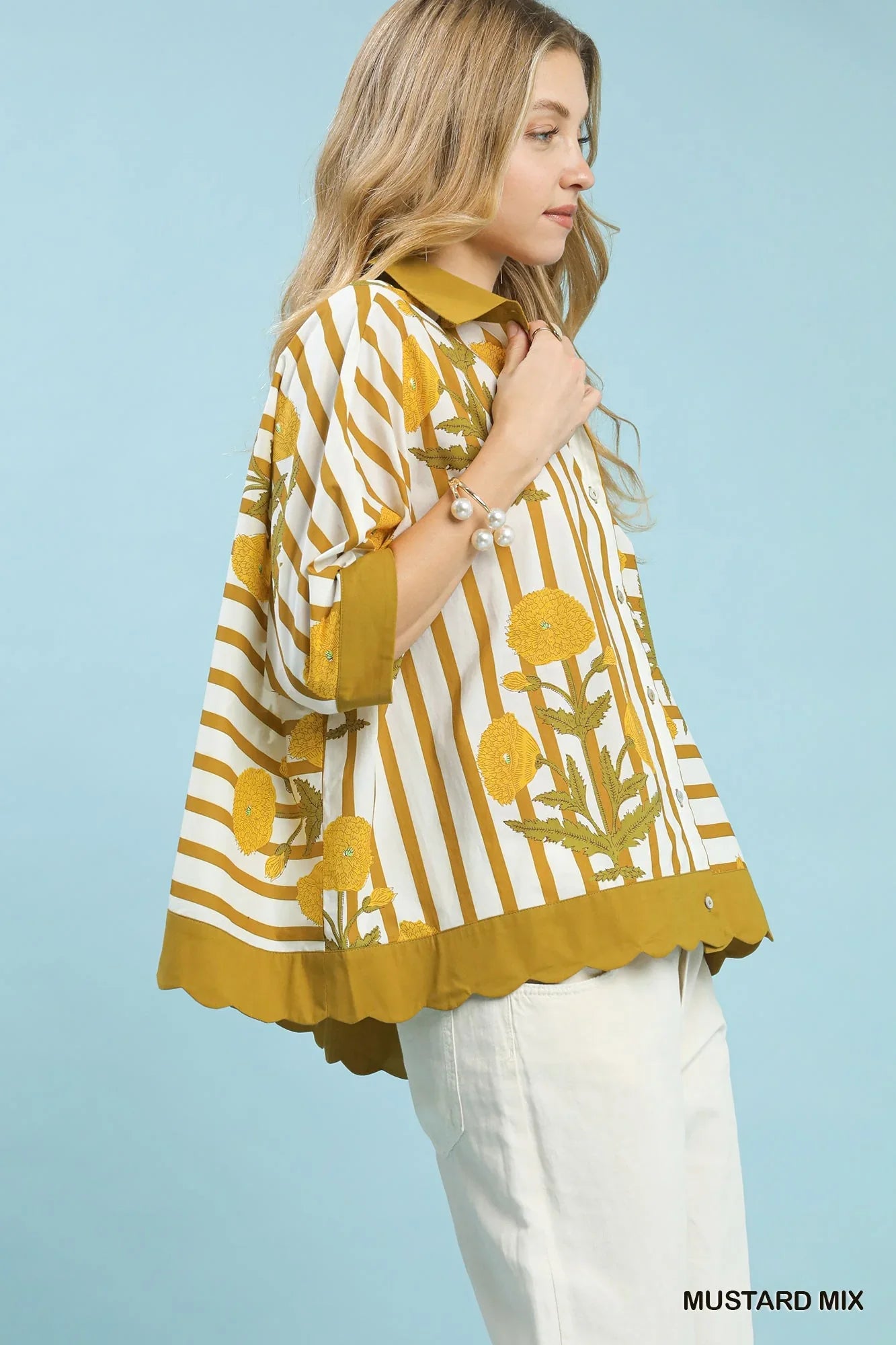 Woman wearing a mustard yellow floral striped blouse with wide sleeves and white pants