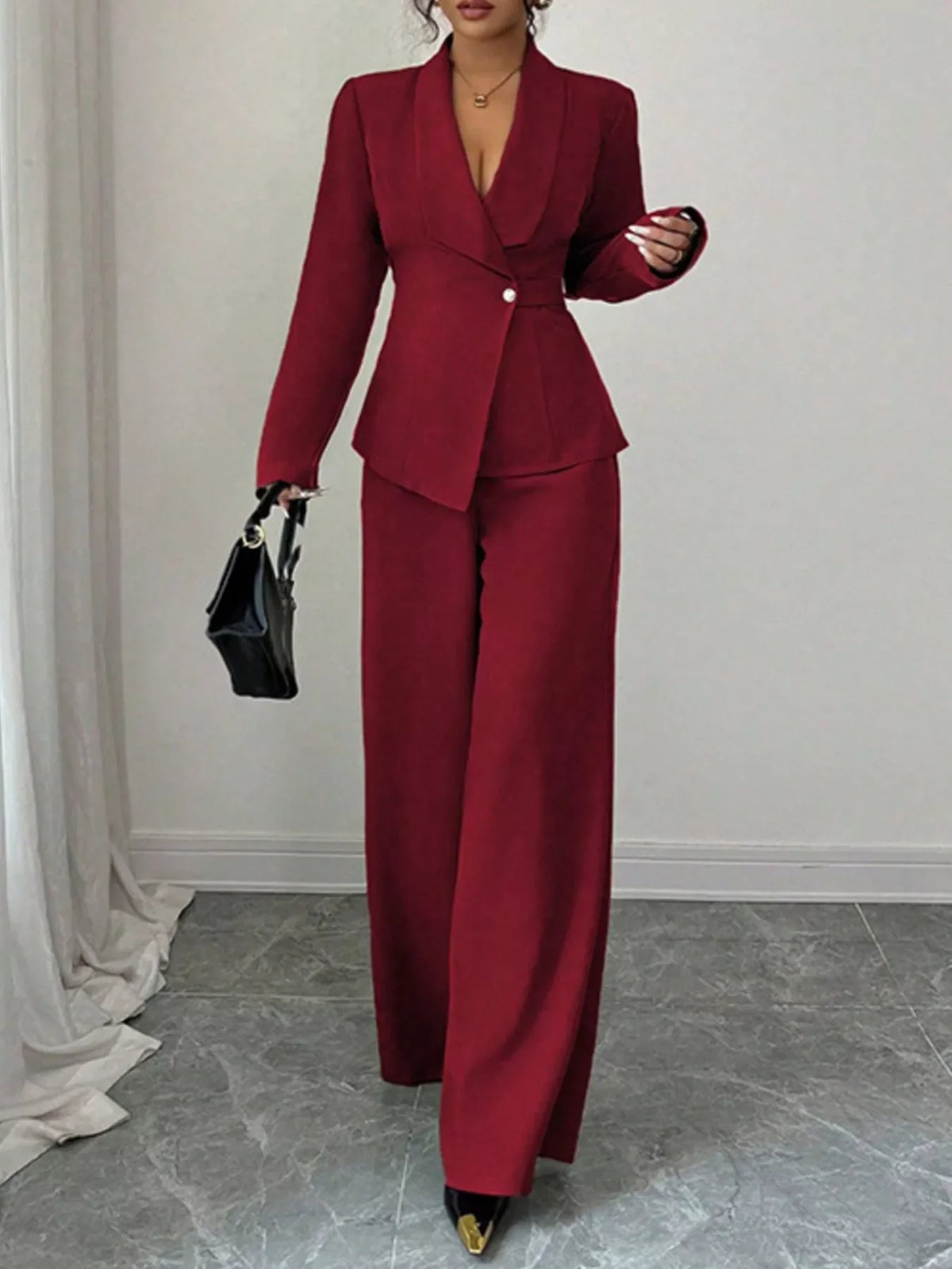 Woman in a burgundy pantsuit with blazer, wide-leg trousers, black handbag, and heels