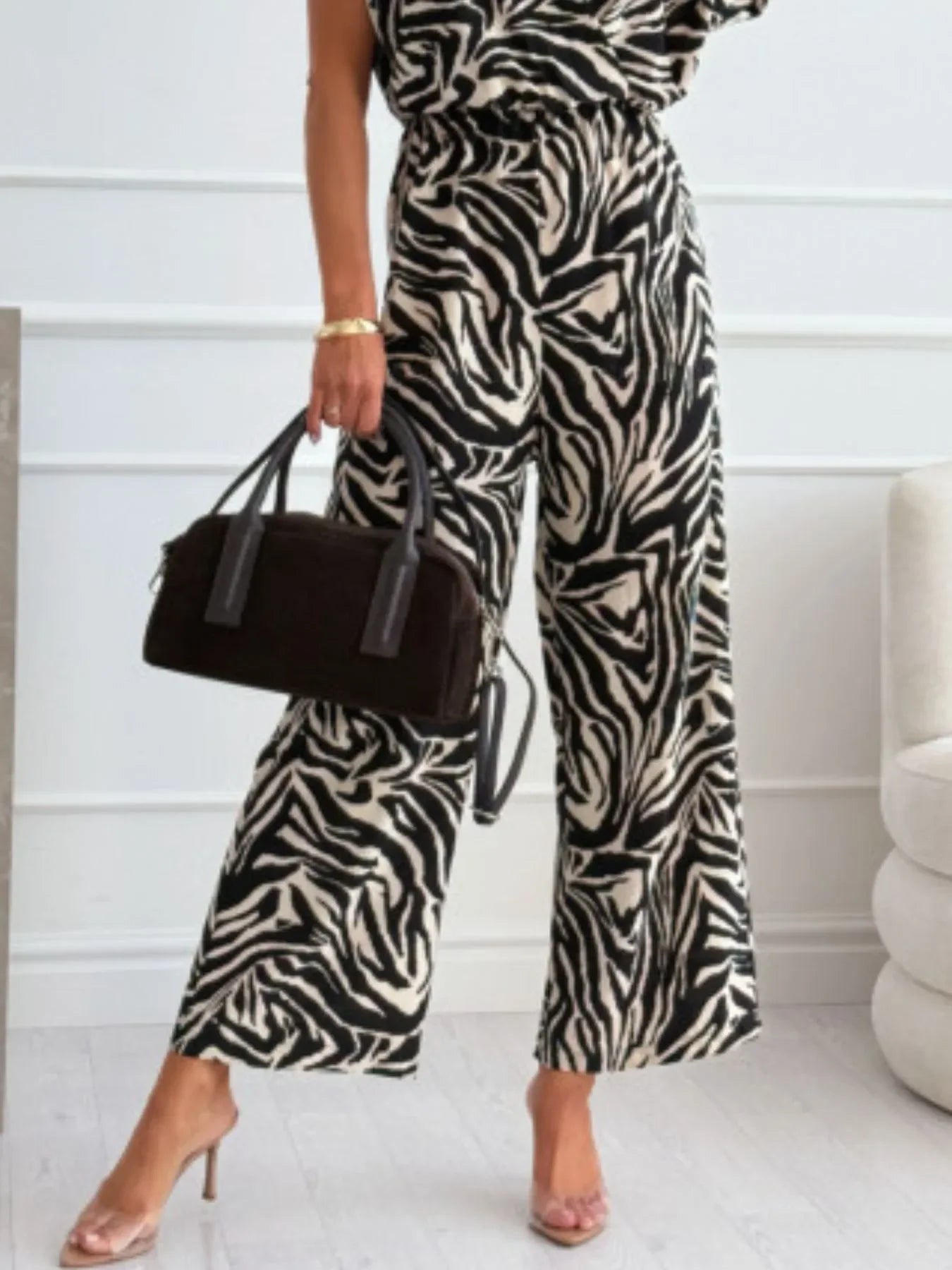Woman wearing black and white zebra print wide-leg pants with clear high heels and holding a black handbag