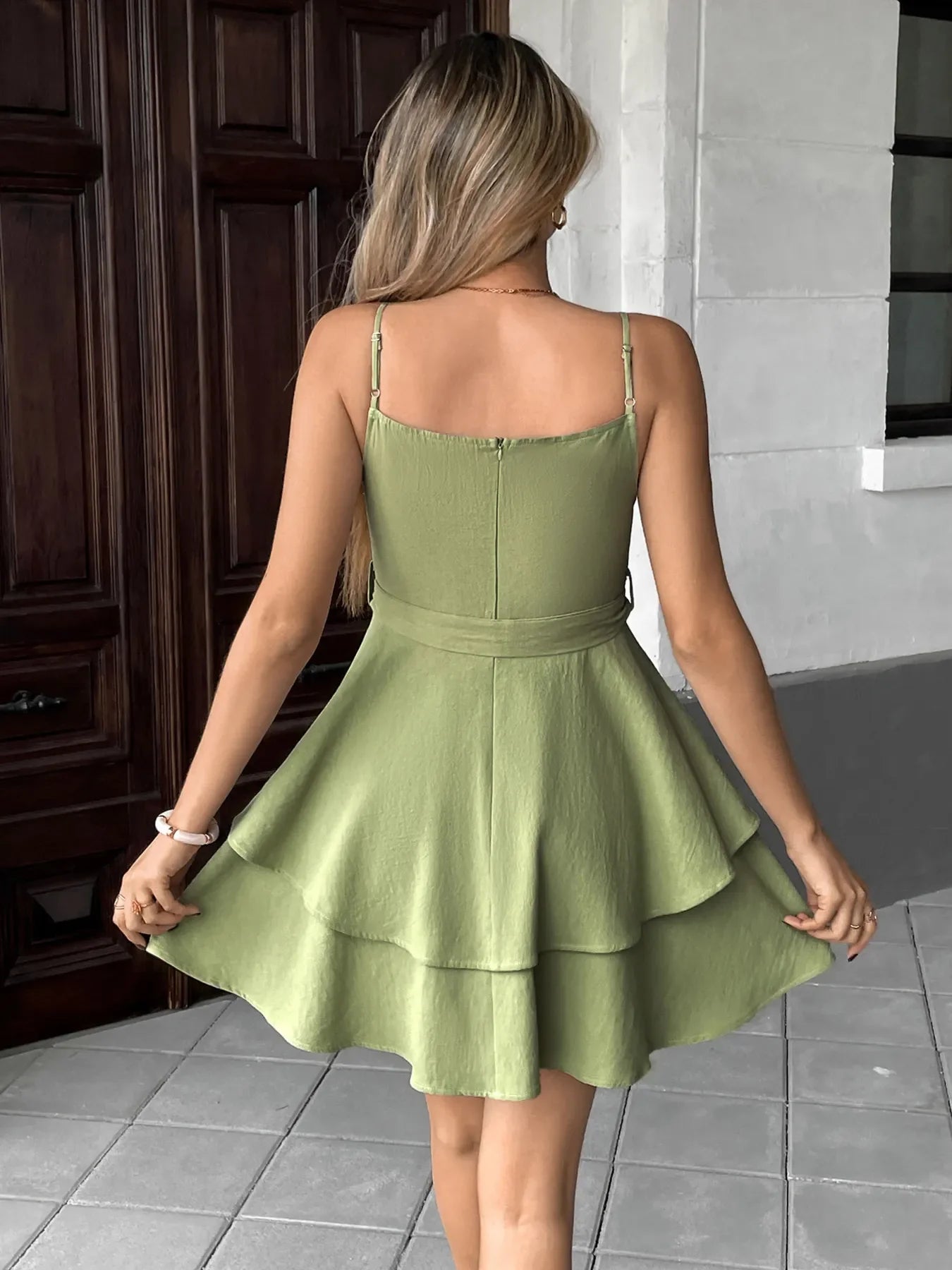 Woman in a light green sleeveless layered mini dress with spaghetti straps, viewed from the back
