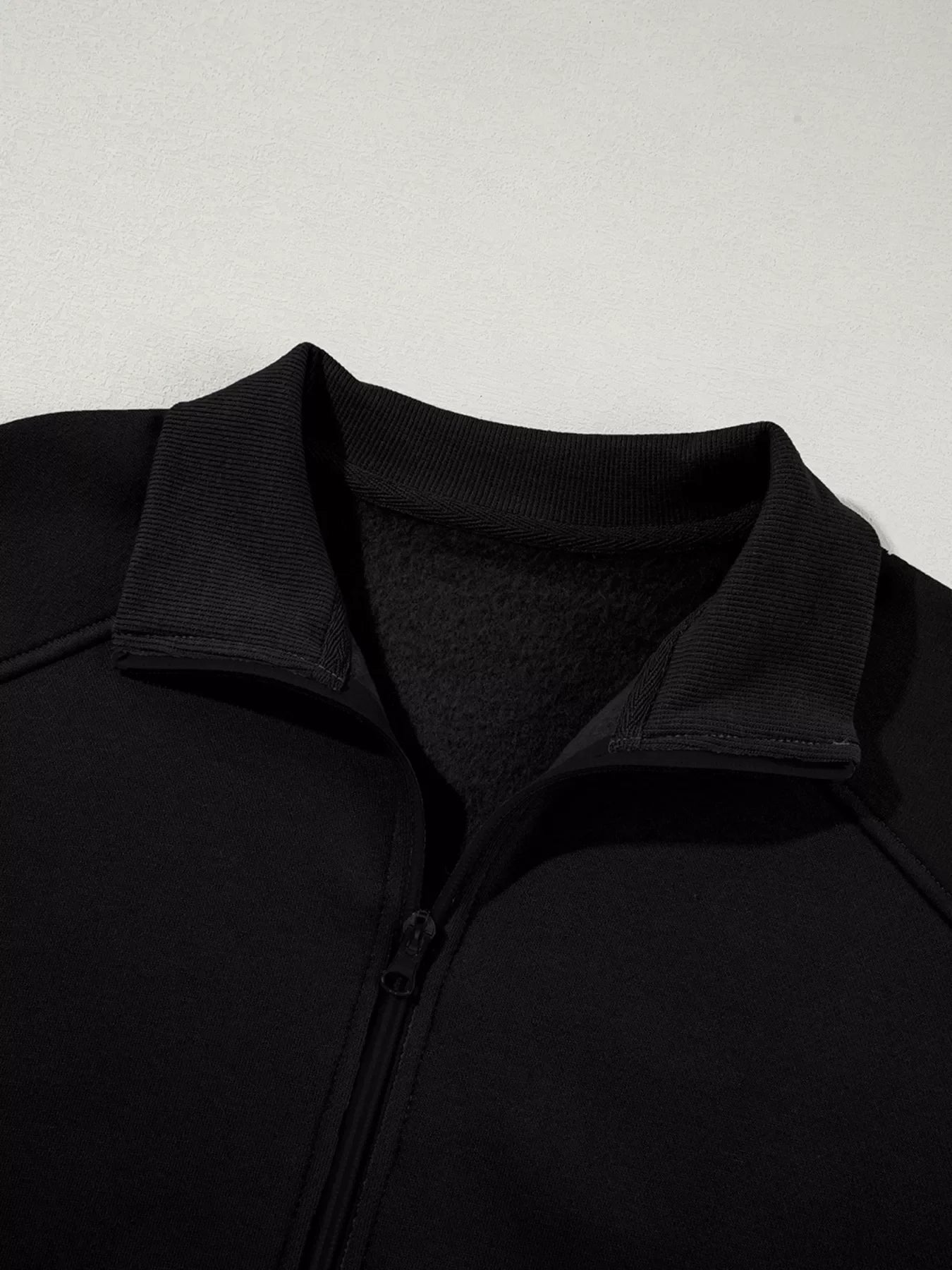Close-up of black zip-up fleece jacket with ribbed collar on gray background