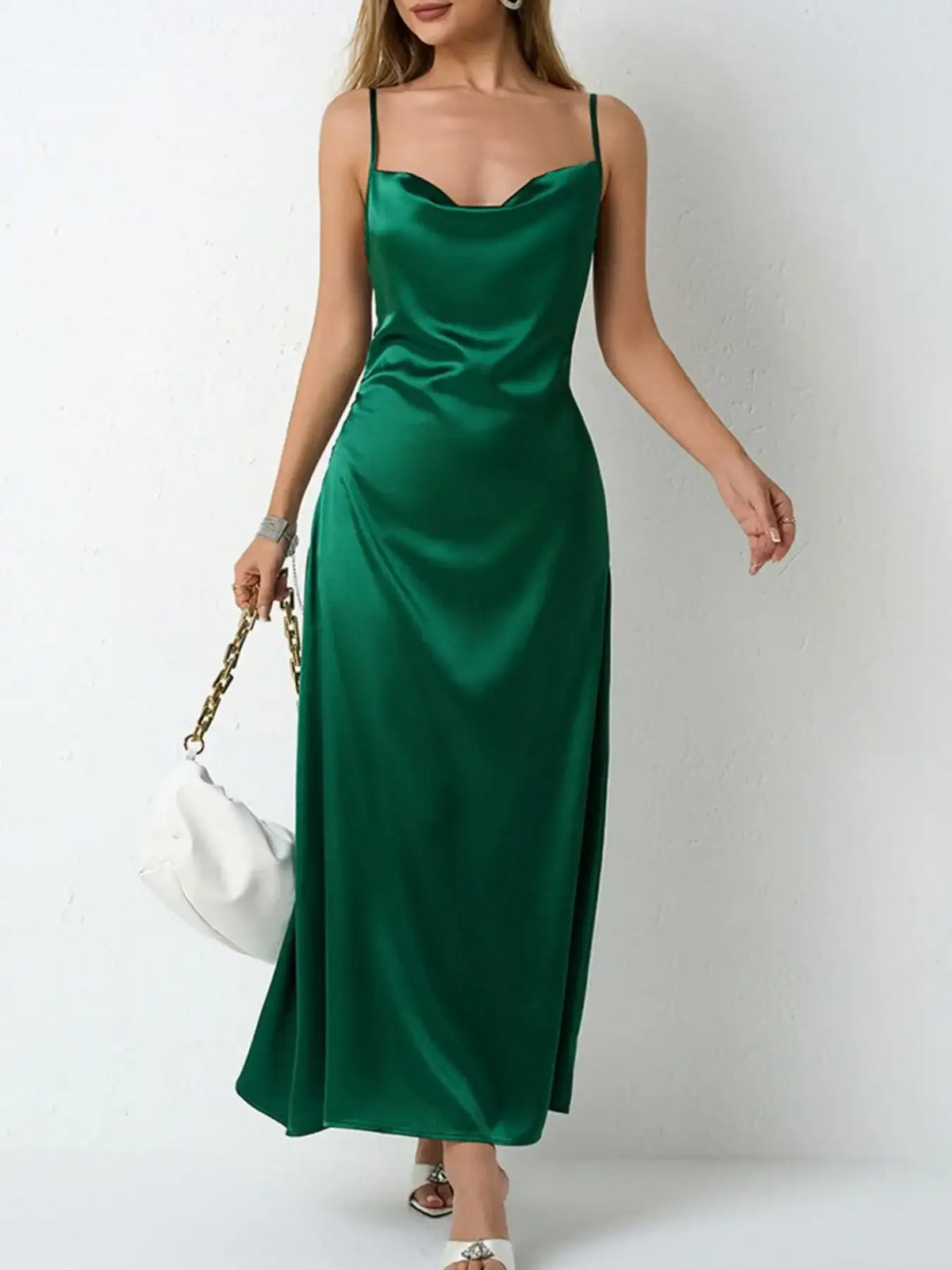 Woman wearing an emerald green satin cowl neck slip maxi dress from Evie's Dreamland with a white handbag.