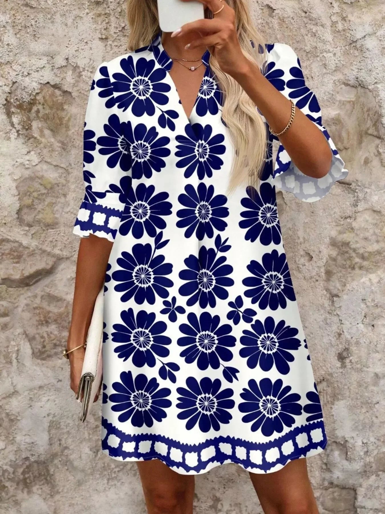 Woman in white knee-length dress with navy blue floral print and half sleeves holding a clutch