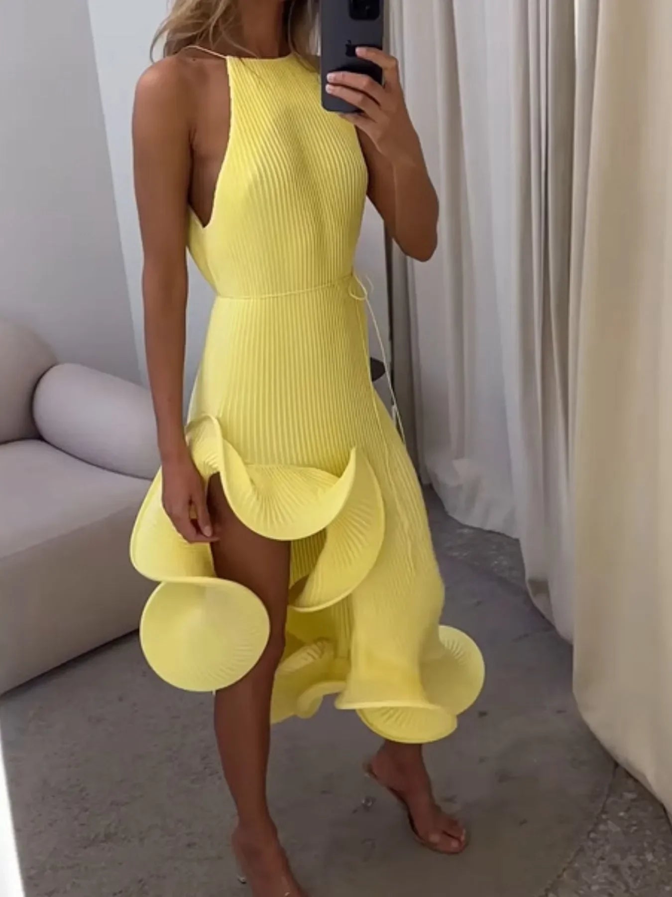 Woman wearing a yellow textured ruffle dress taking a mirror selfie in a modern room