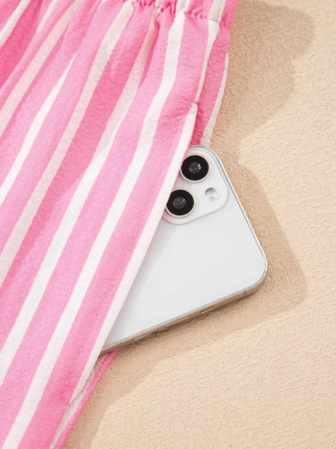 White smartphone partially inside a pink and white striped fabric pocket on a textured surface