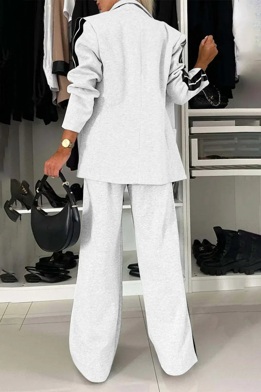 Woman in cozy light gray loungewear set with black stripes on sleeves, holding black handbag indoors