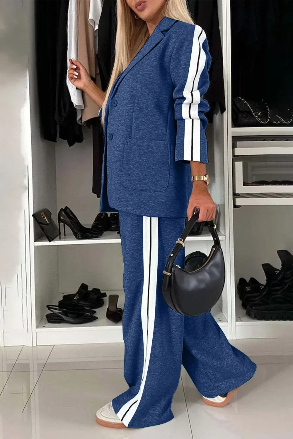 Woman in blue two-piece casual suit with white stripes holding black handbag in modern closet