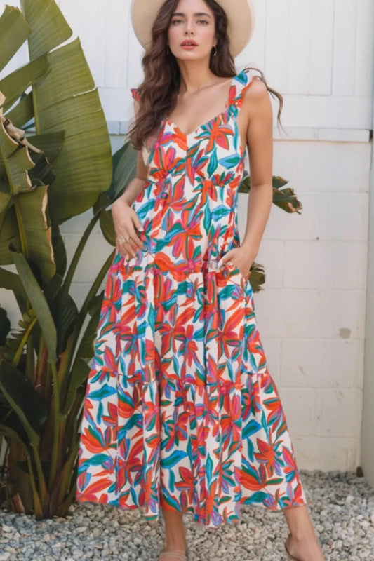 Woman in colorful floral maxi dress with ruffle sleeves and pockets, wearing a sunhat outdoors.