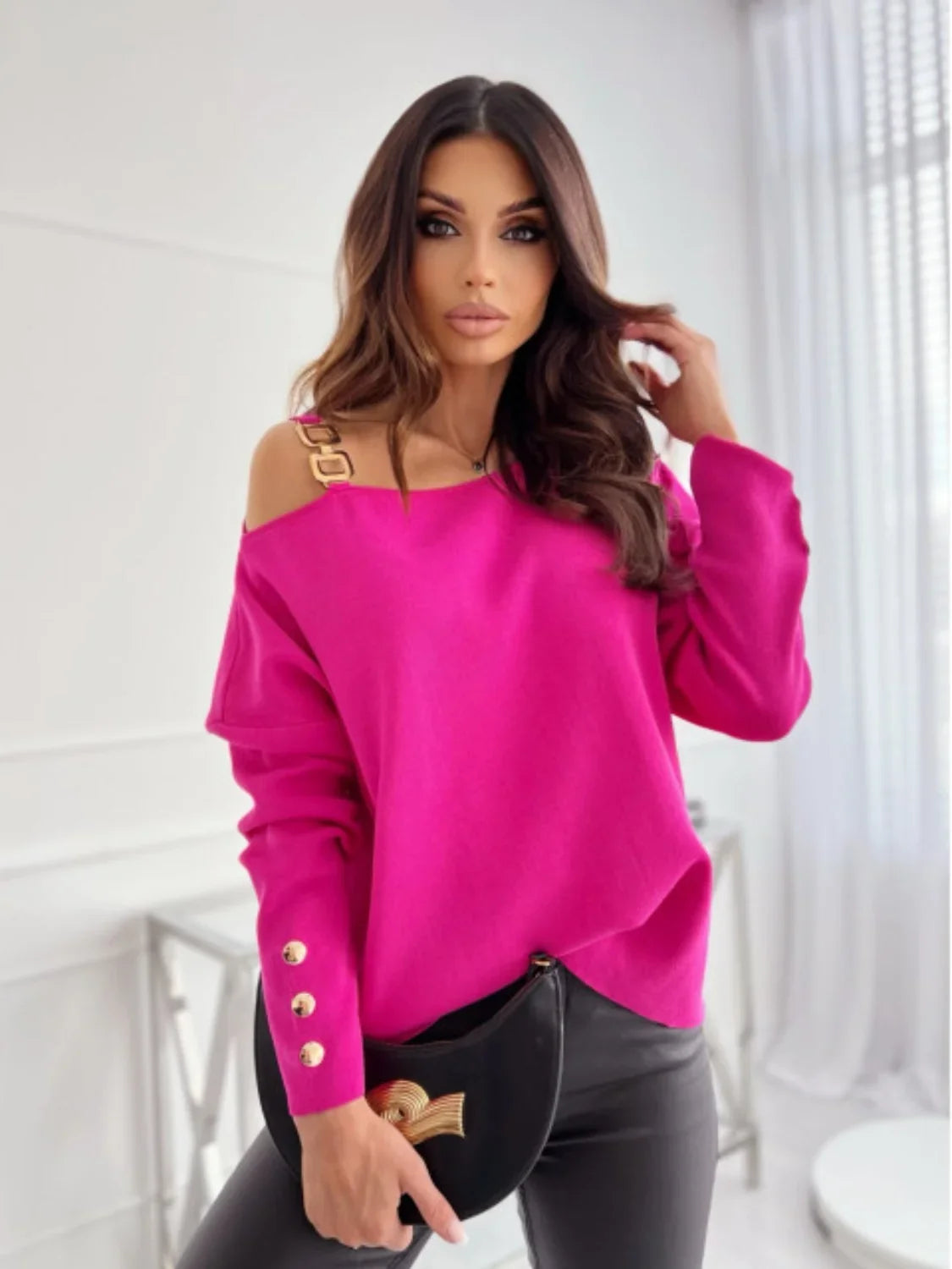 Woman wearing a bright pink off-shoulder sweater with gold accents and black leather pants