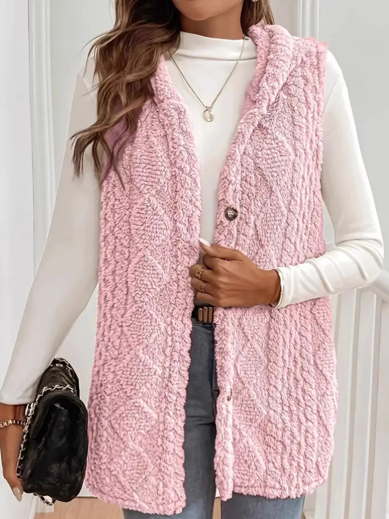 Woman wearing soft pink fuzzy textured sleeveless vest with white long sleeve top and jeans