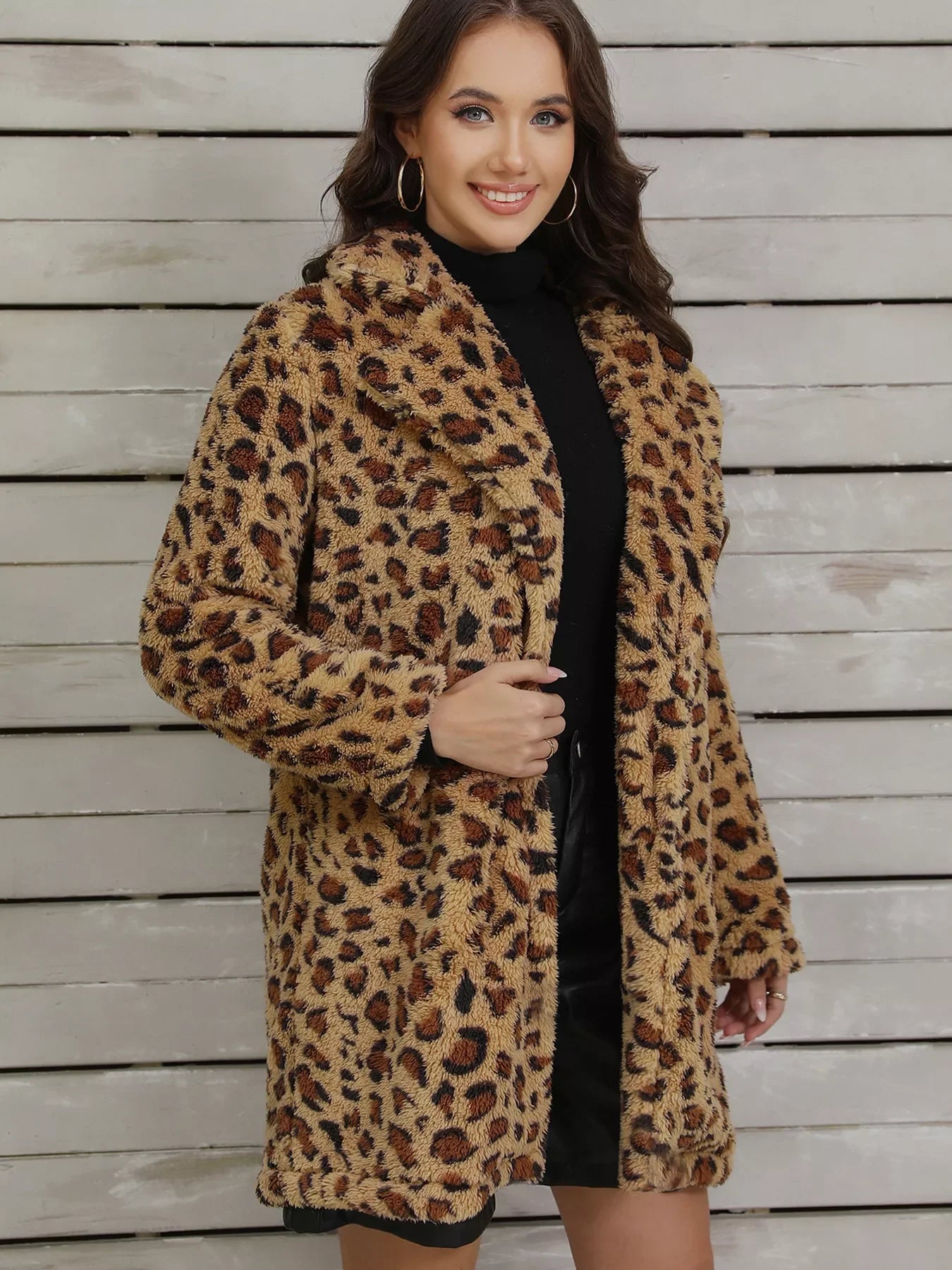 Woman wearing a leopard print faux fur coat over a black turtleneck and skirt, standing against a wooden wall